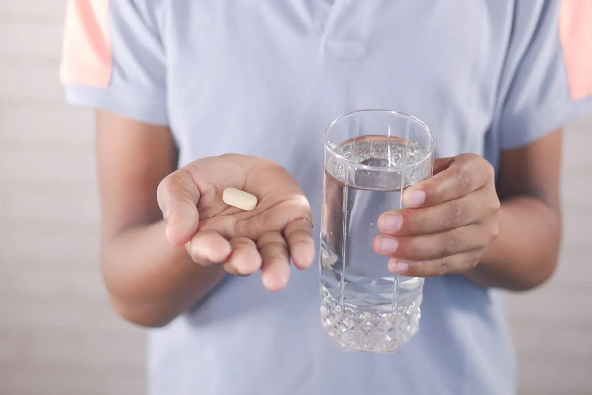 Open palm holding a single tablet beside a glass of water