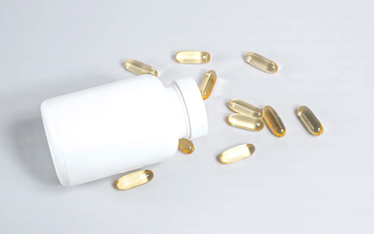 Golden softgel capsules spilling from a plain white bottle on a white surface