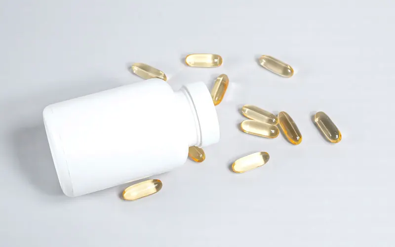 Golden softgel capsules spilling from a plain white bottle on a white surface