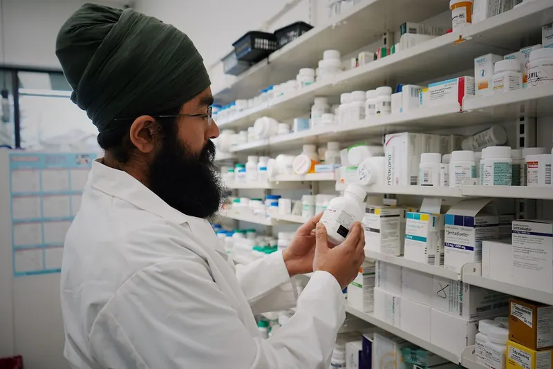 Pharmacist examining a medicine bottle in front of well-stocked pharmacy shelves