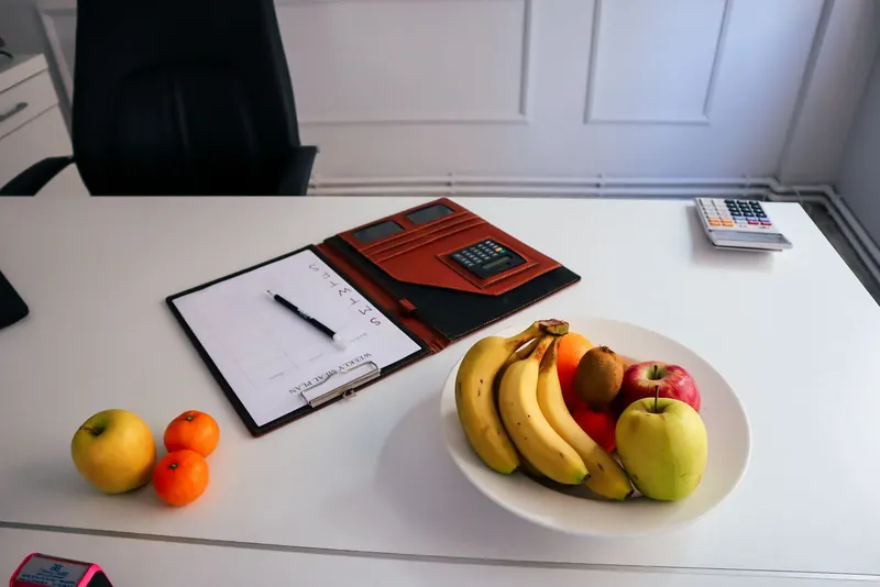 Planner, pen and a bowl of fresh fruit on a white desk