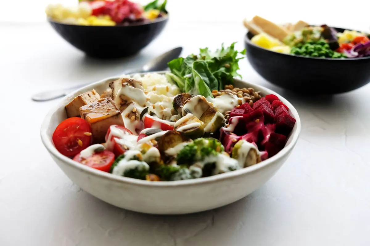 Colorful bowl of fresh vegetables, greens and grains on a white table