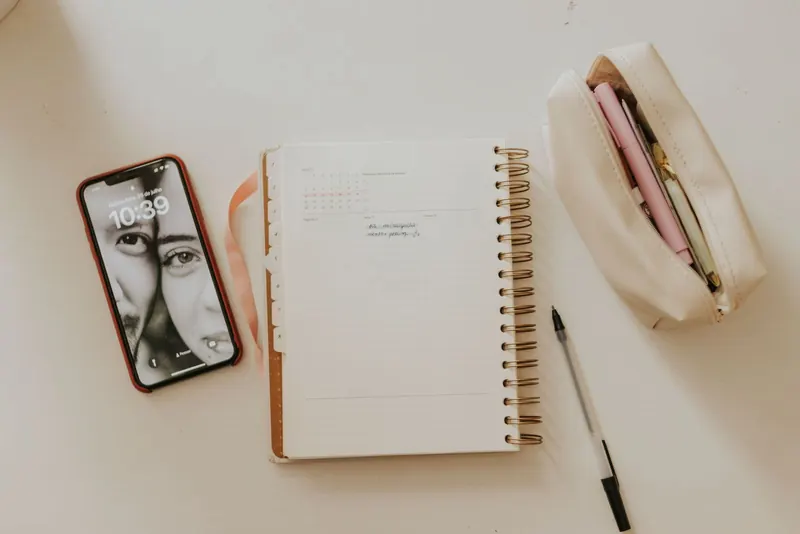 Flat lay of a smartphone, open spiral planner, pen and pencil case on a light desk