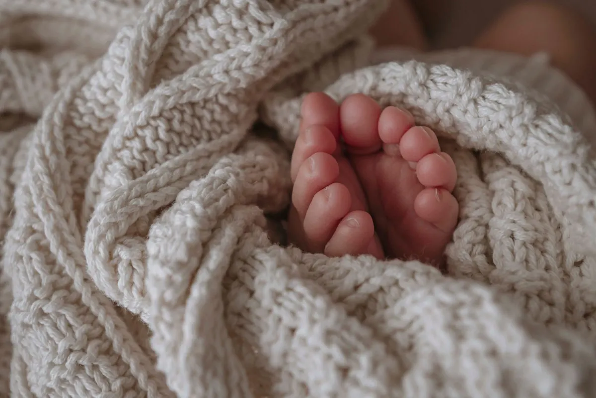 Newborn baby's feet tucked into a soft cream knitted blanket