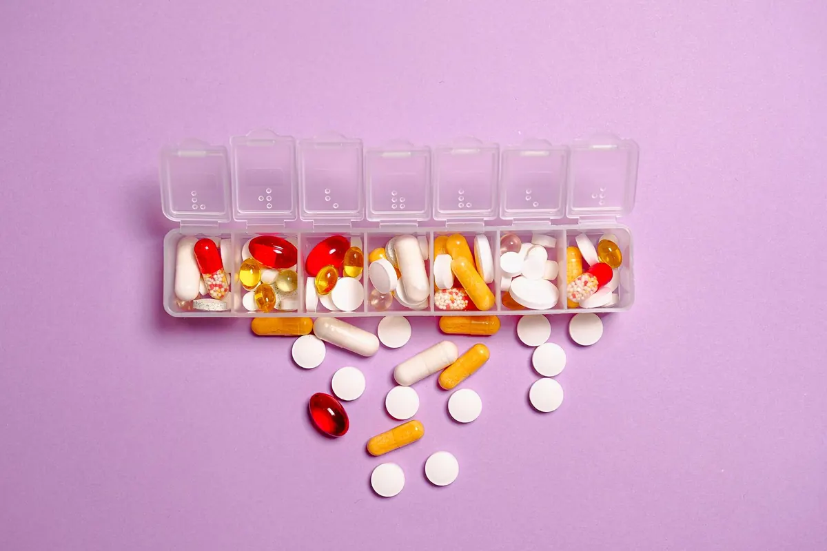 Clear daily pill organizer filled with capsules and tablets on a lilac background