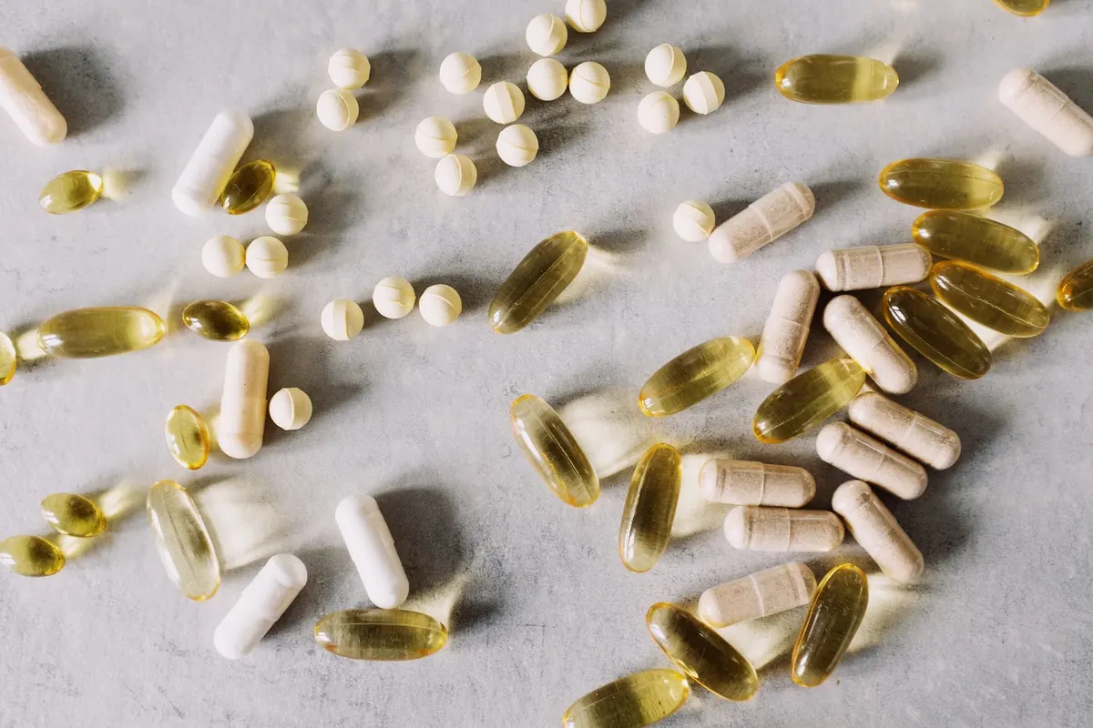 Close-up of assorted vitamin capsules, softgels and tablets scattered on a light surface