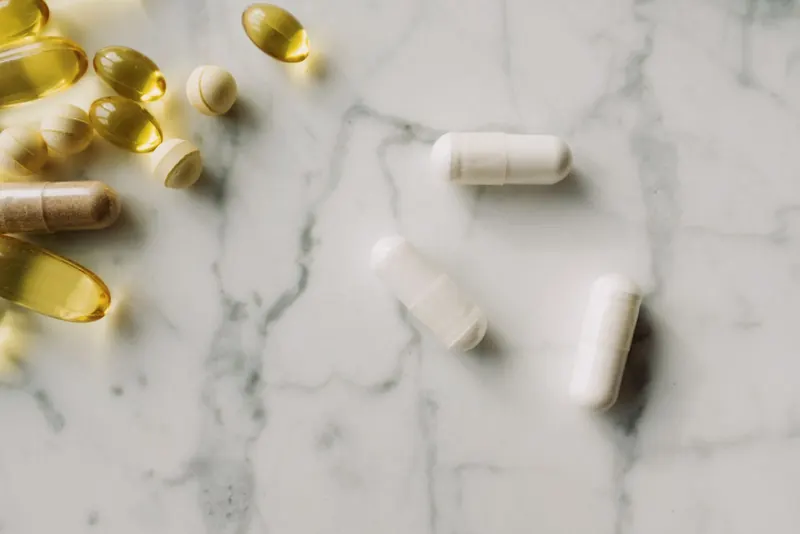 Close-up of white supplement capsules and golden softgels on a white marble surface