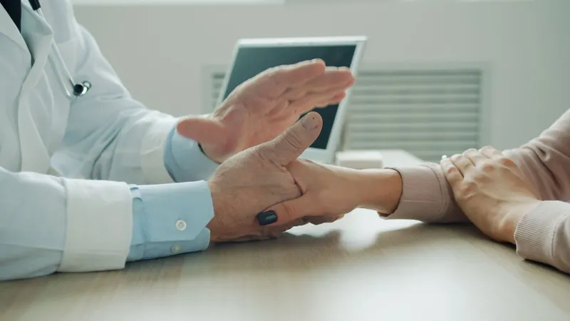 Doctor holding a patient's hand and wrist across a desk during a consultation