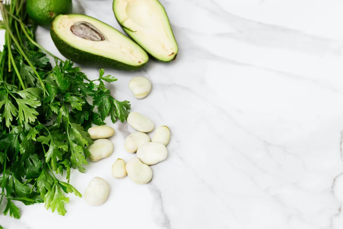 Overhead view of fresh parsley, avocado halves and broad beans on white marble