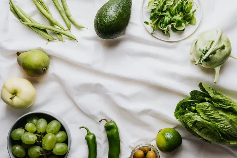 Green beans, avocado, lettuce, lime, grapes and other green produce laid out on a white cloth