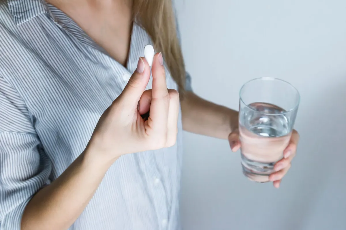 Woman holding a white tablet in one hand and a glass of water in the other