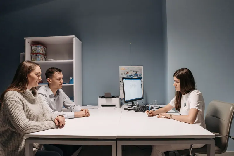 Couple seated at a table talking with a clinician in a bright consultation room