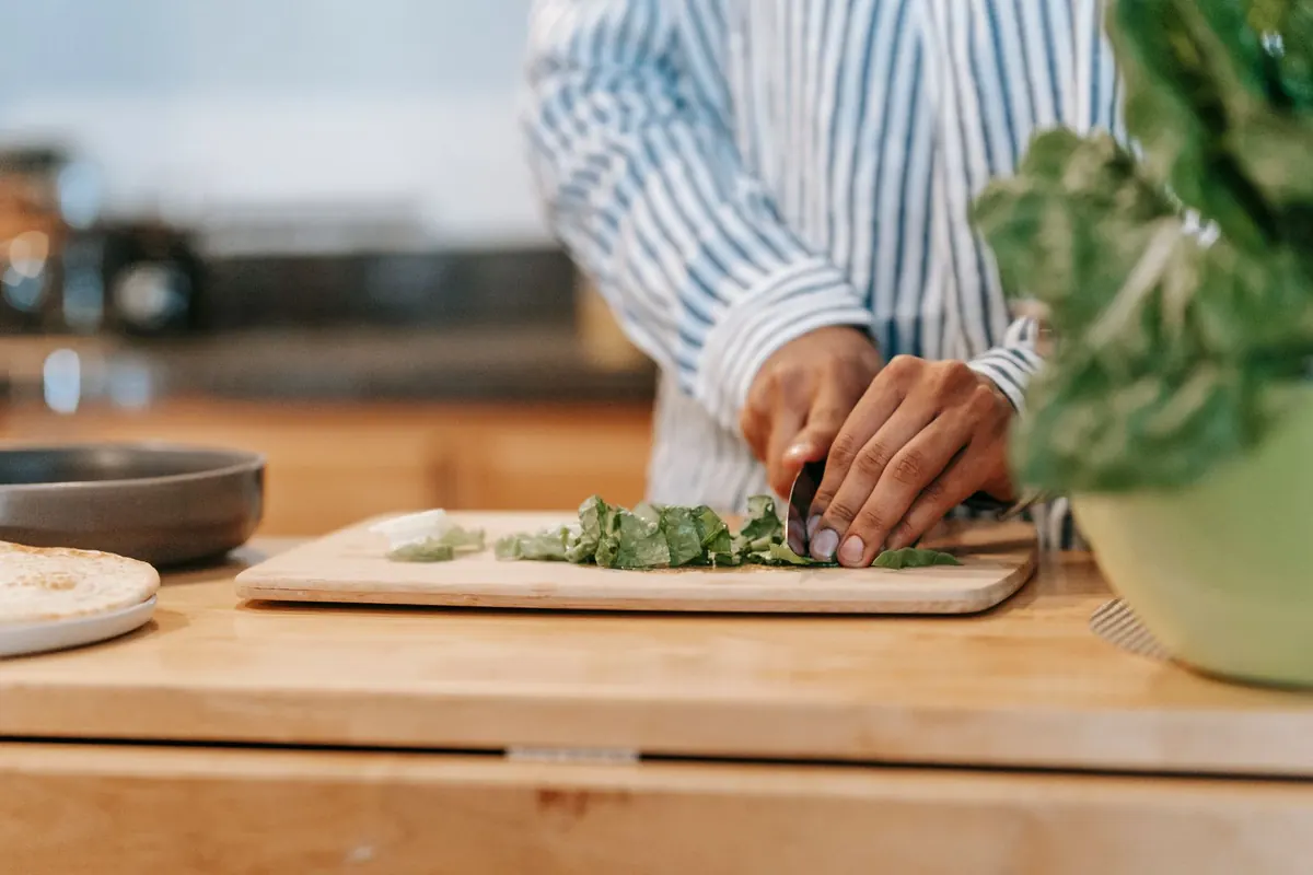 Man chopping fresh spinach leaves on a wooden board in a home kitchen