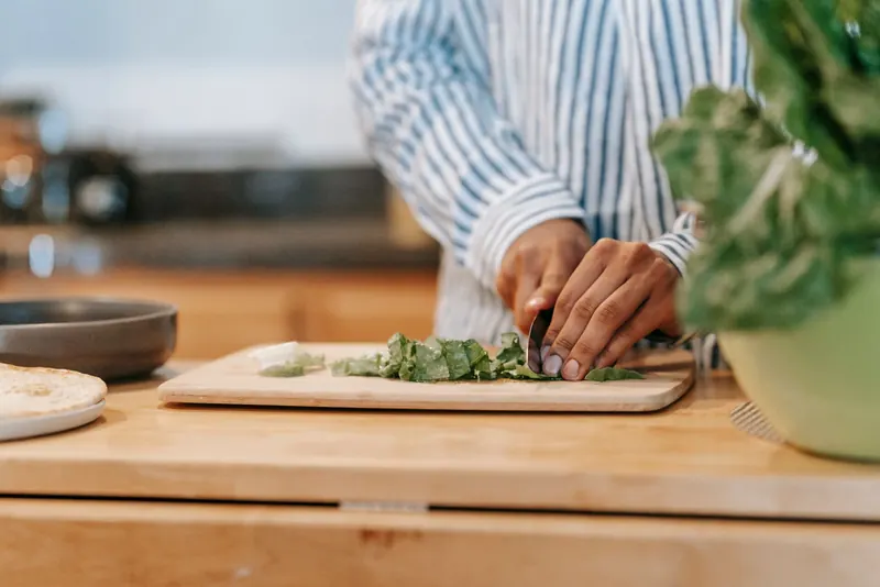 Man chopping fresh spinach leaves on a wooden board in a home kitchen