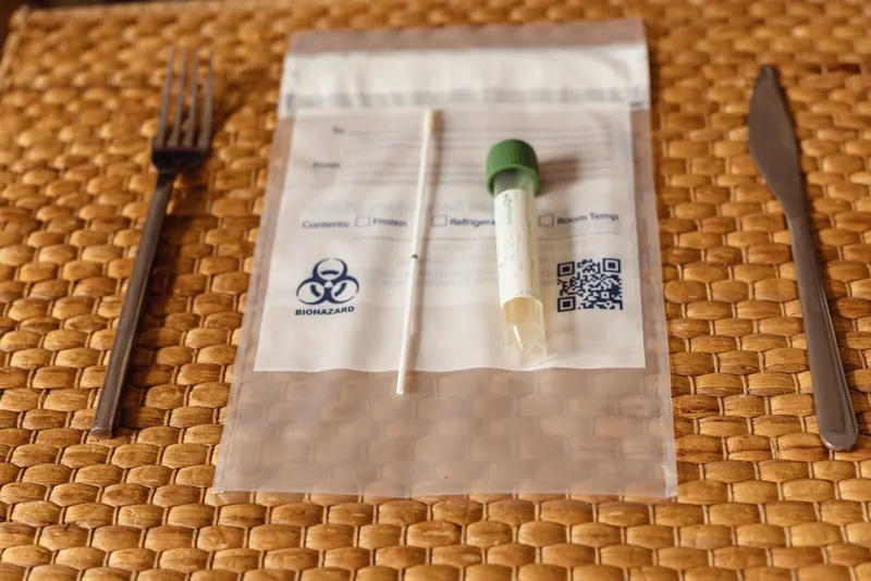 Home sample collection kit with swab and tube in a specimen bag on a woven placemat