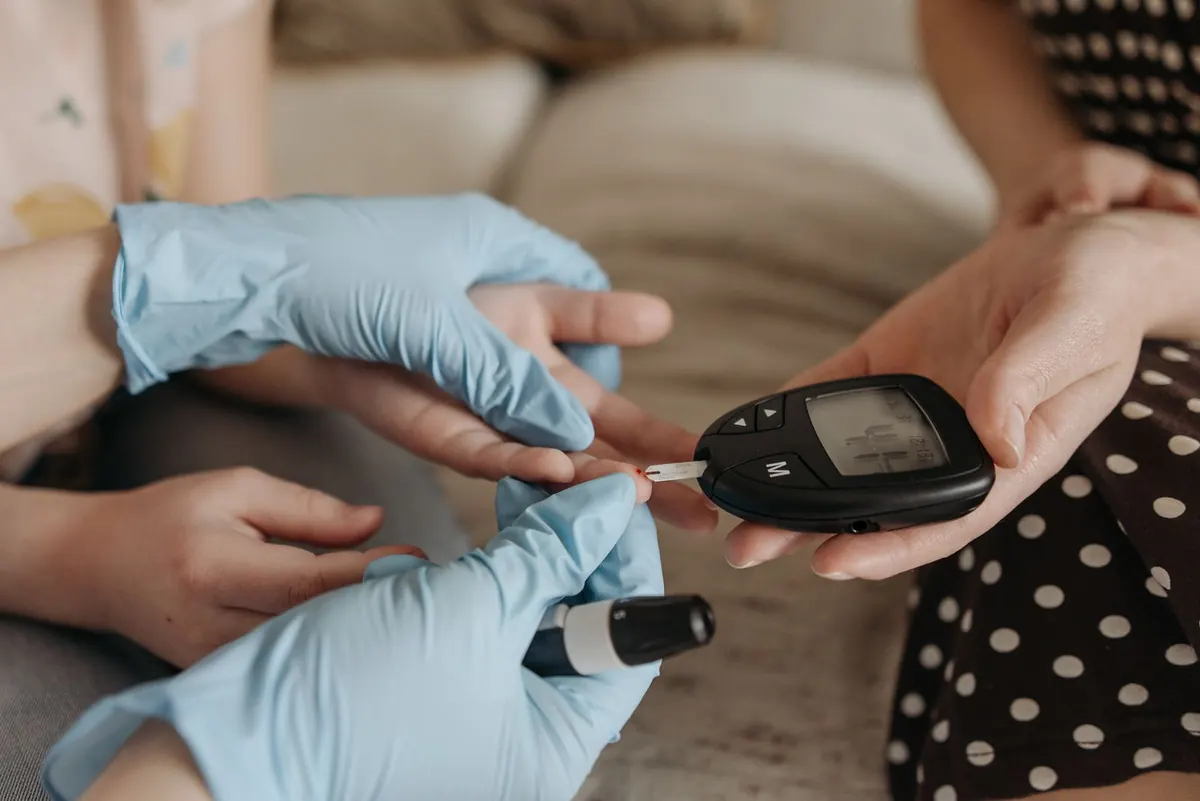 Gloved hands helping a woman with a finger-prick test using a handheld meter at home