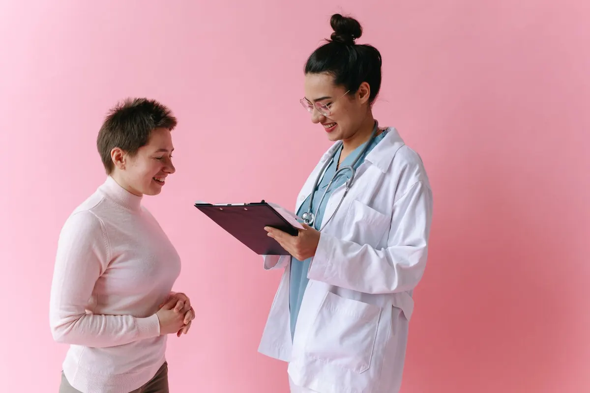 Smiling woman listening as a clinician in a white coat reviews results on a clipboard