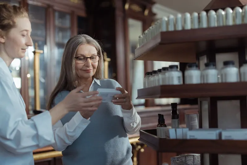 Pharmacist in a white coat helping an older woman look at a product in a pharmacy