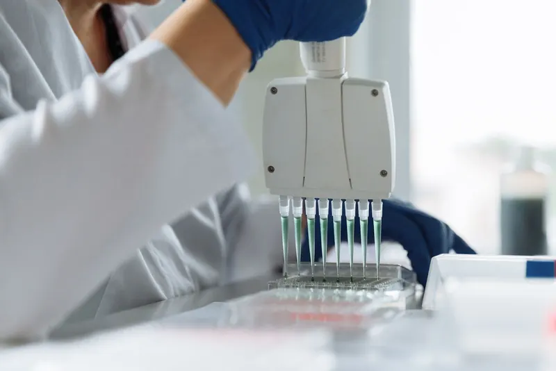 Scientist in a lab coat using a multichannel pipette in a bright genetics lab